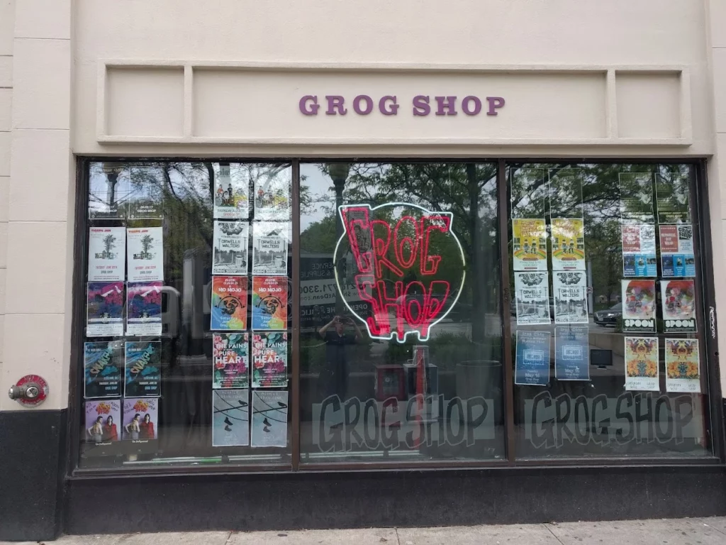 grog(3) Front window of Grog Shop music venue covered in colorful show posters and a neon sign, a staple in the local scene known for supporting LGBTQ+ artists and trans-inclusive events.